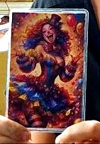 Hands holding the vivid clown card up close, a burst of red, blue and gold