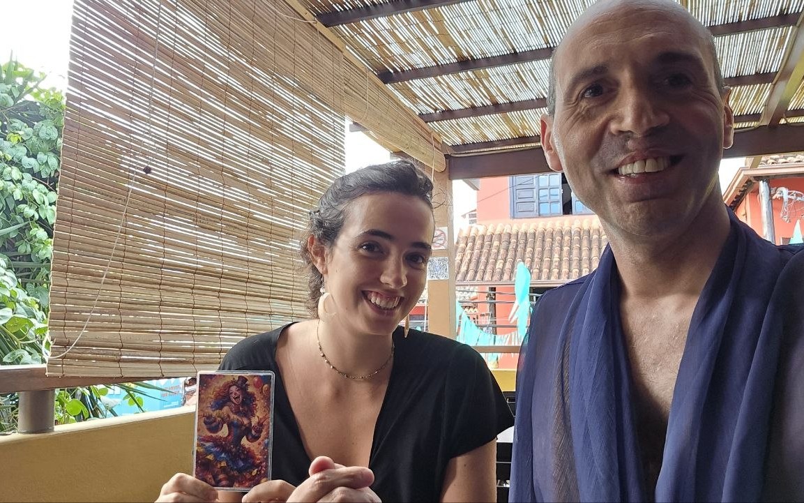 Dino and Lua smiling on a bamboo-shaded balcony, Lua holding the vivid clown card